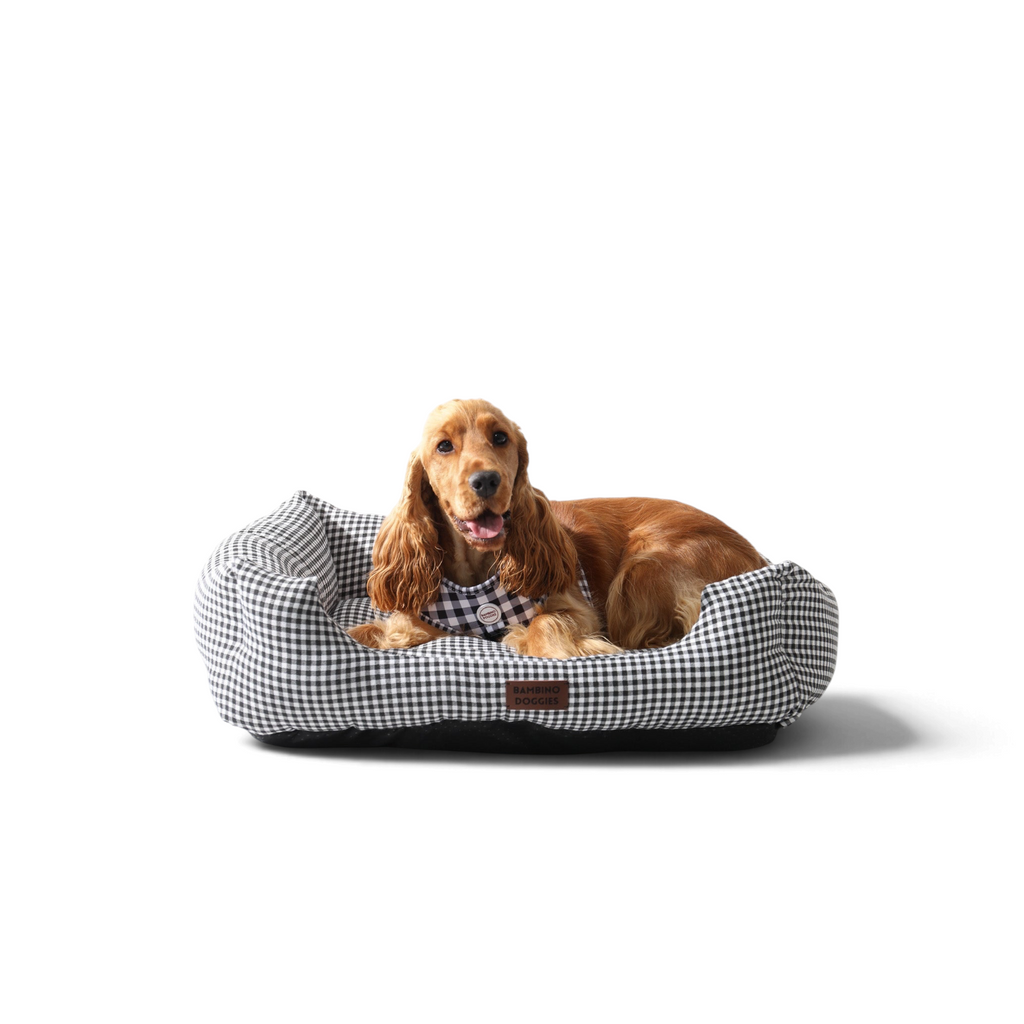 Cama para perros Bambino Doggies con estampado vichy negro y blanco, con un perro cocker spaniel descansando en ella.
